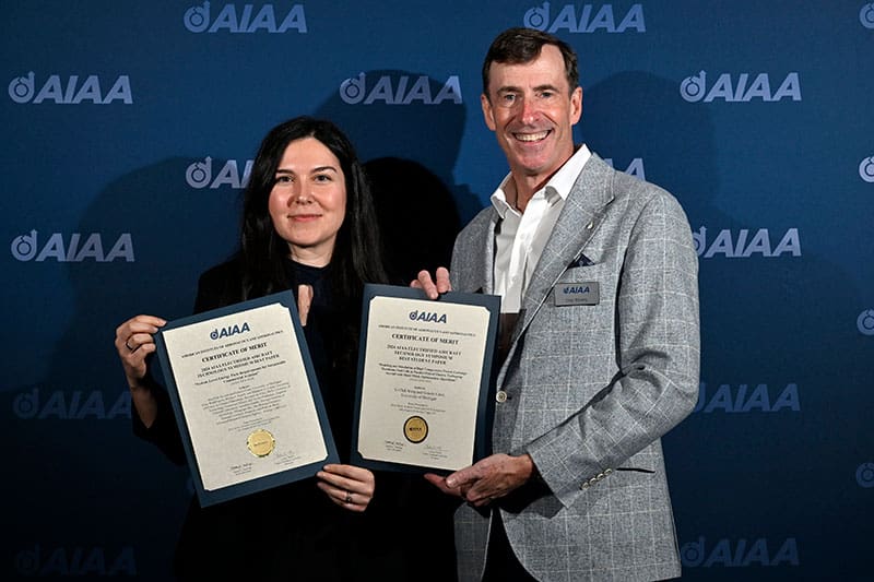 photo of Gökçin Çınar, a woman with dark hair, holding up a paper certifying that she received the Lawrence Sperry Award next to a tall man who is also holding an award