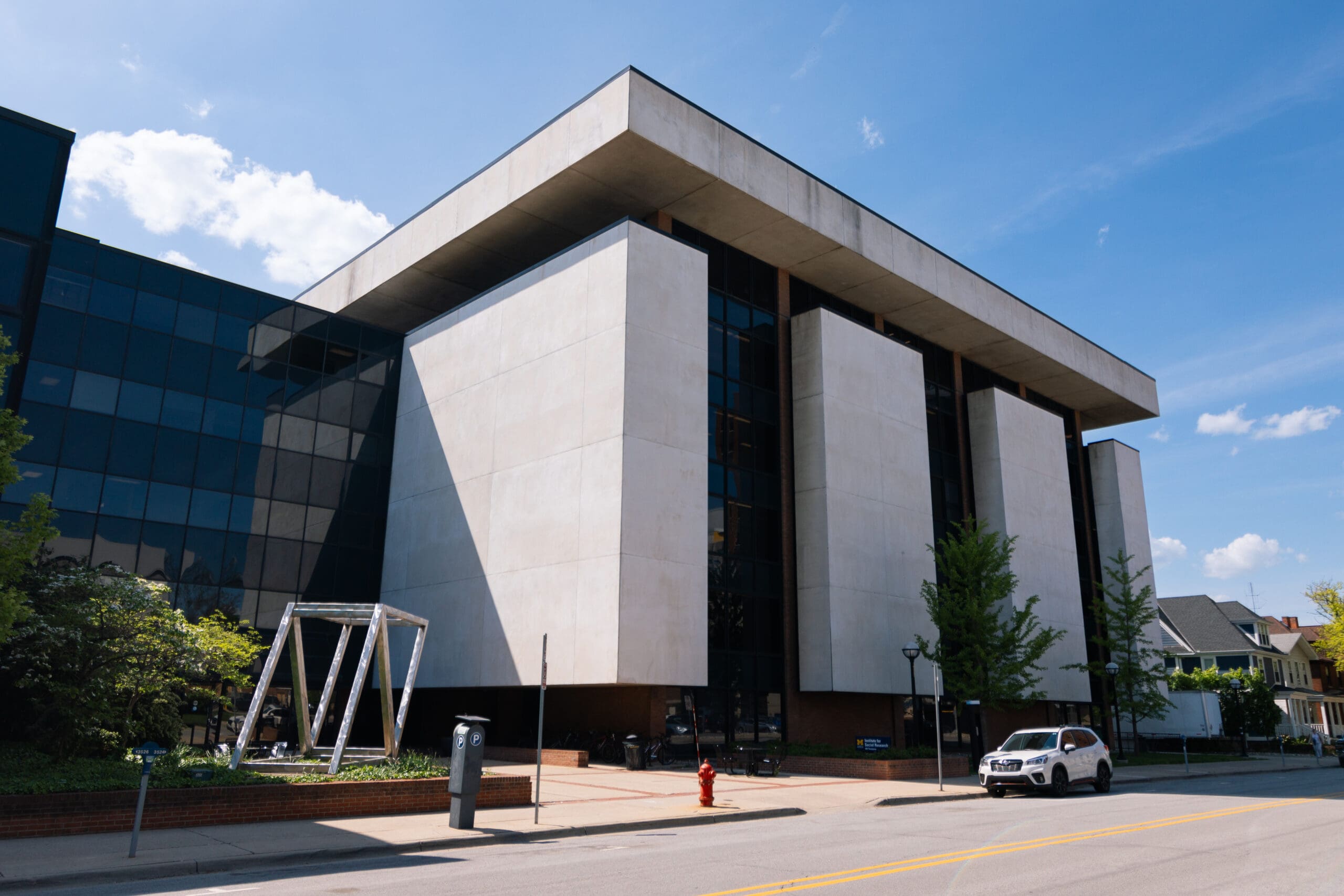 The Institute for Social Research, a large white stone building with bays of black windows and “Convergence,” a metal statue made of large triangles resting against one another on the sidewalk outside.