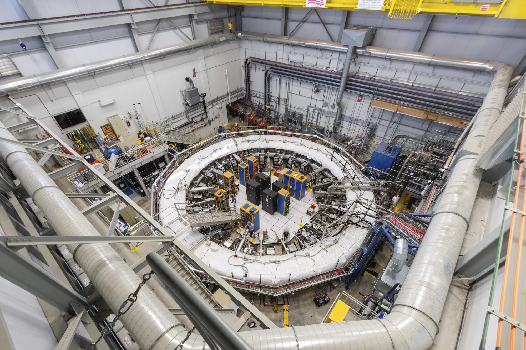 An aerial view within a large industrial space showing the Muon g-2 experiment at the U.S. Department of Energy’s Fermilab